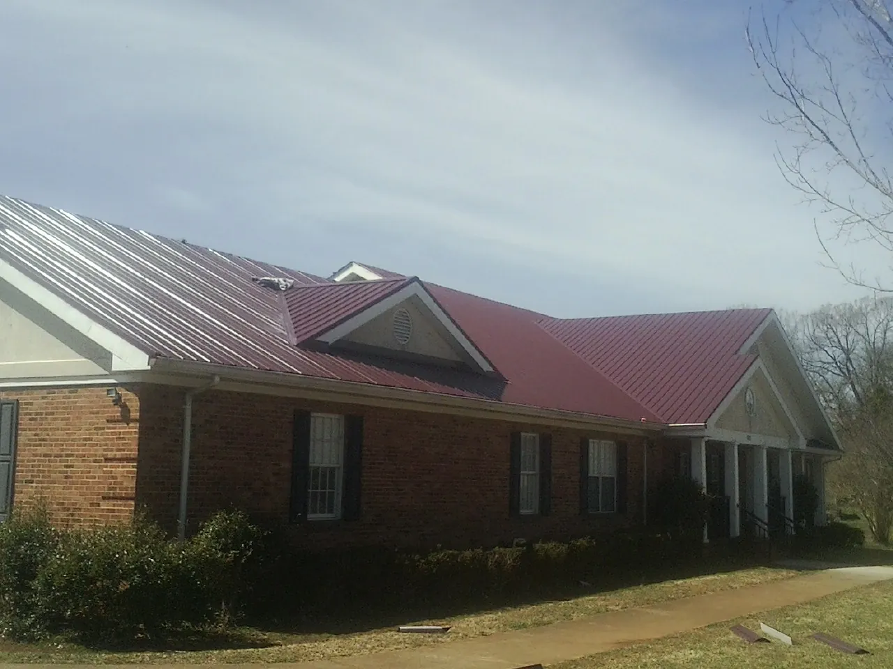 Red metal roof with gabled entries on a long brick building, from a Hail Damage Roof Repair job in Elbe