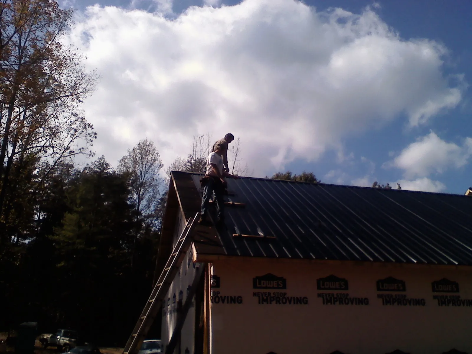Roofer fastening dark metal panels high against a cloudy sky, from a Roof Inspection job in Elbe