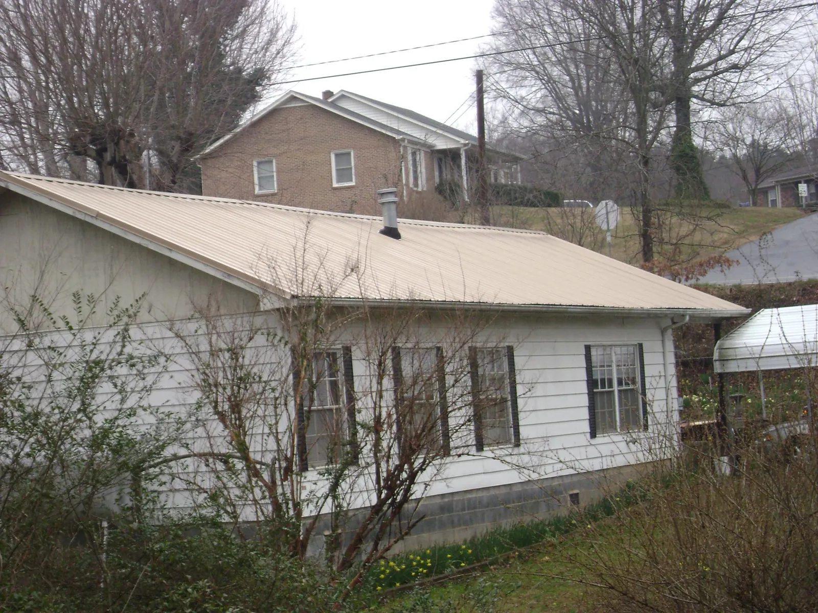 Tan metal roof on a white sided house set into a hillside — Commercial Roofing by Roofing Brothers in Elbe