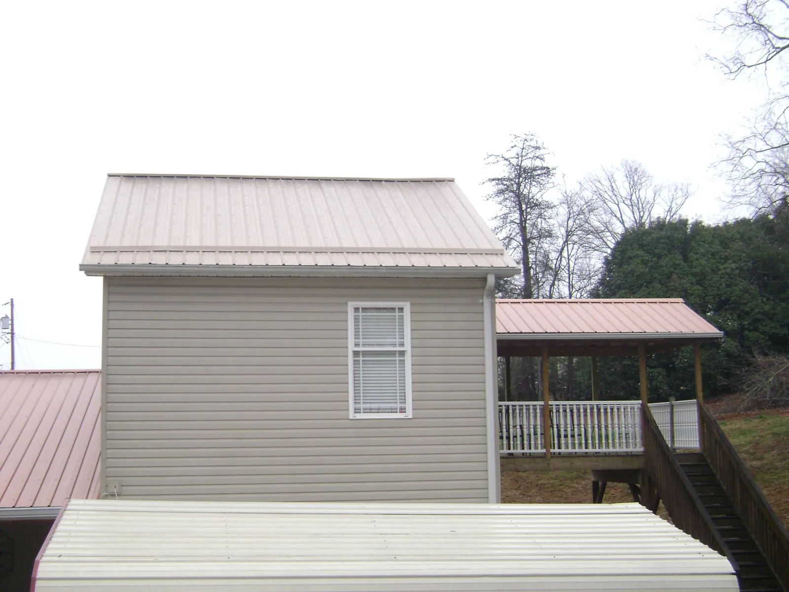 Tan metal roofs on a two story addition and attached porch, from a Roof Replacement job in Elbe